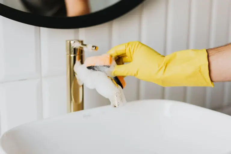 Gloved hand polishing a gold bathroom faucet