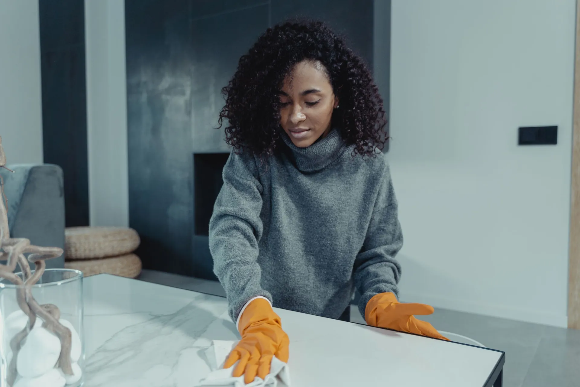 Cleaner in gloves wiping a glass coffee table in a bright living room