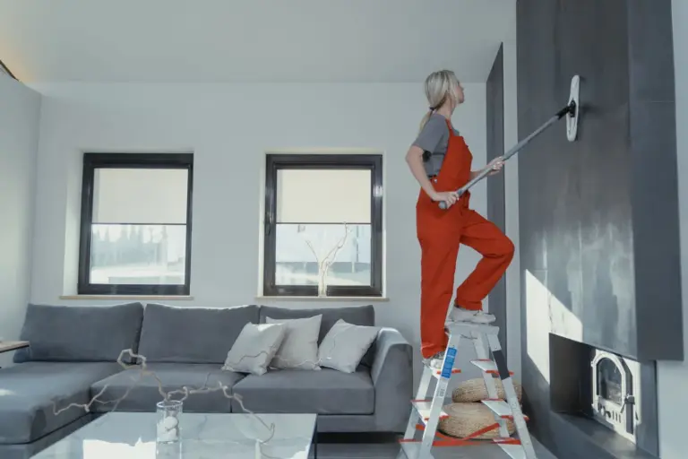 Cleaner on a step ladder wiping a living room wall with a mop