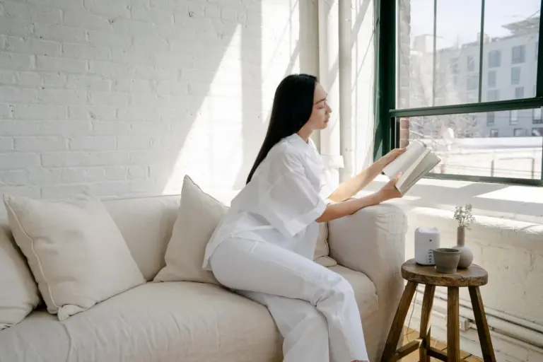 Woman reading on a white sofa in a sunlit, tidy living room