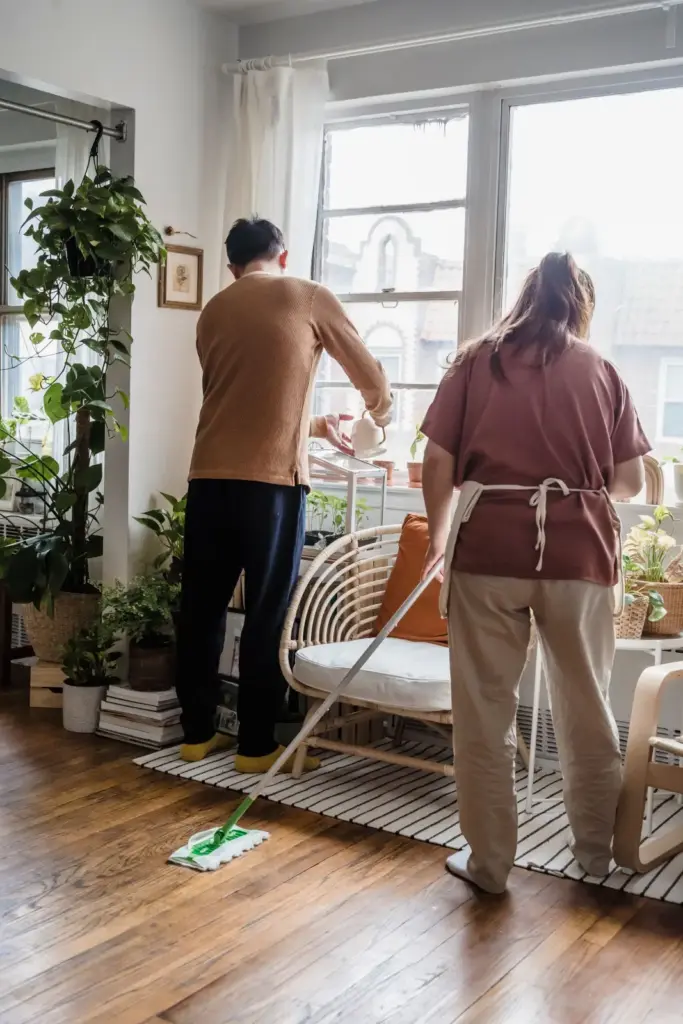 Two people cleaning a plant-filled living room together